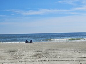 A beach with two people sitting on chairs facing the ocean.