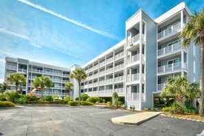 A multi-story hotel with balconies, palm trees, and a parking lot.