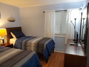 Ein Hotelzimmer mit zwei Betten, einem Schreibtisch mit Computer, einer Lampe und einem Fenster mit Jalousien.