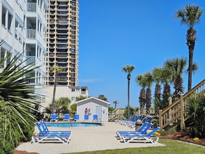 A pool area with blue lounge chairs, a small building, and tall palm trees.
