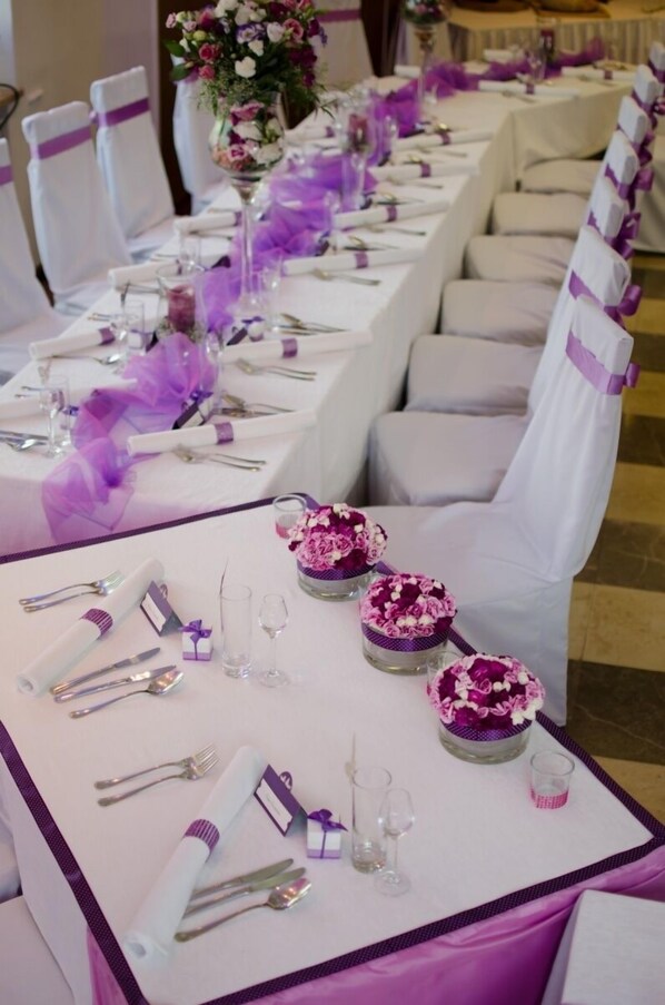 A long banquet table set with white tablecloths, purple sashes, and floral centerpieces.