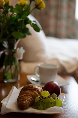 A breakfast setting with a croissant, grapes, and a plum on a plate, a cup of coffee, and a vase with flowers. - West Hotel (Warsaw)