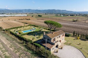 A stone villa with a swimming pool, surrounded by terraced fields and a large tree.