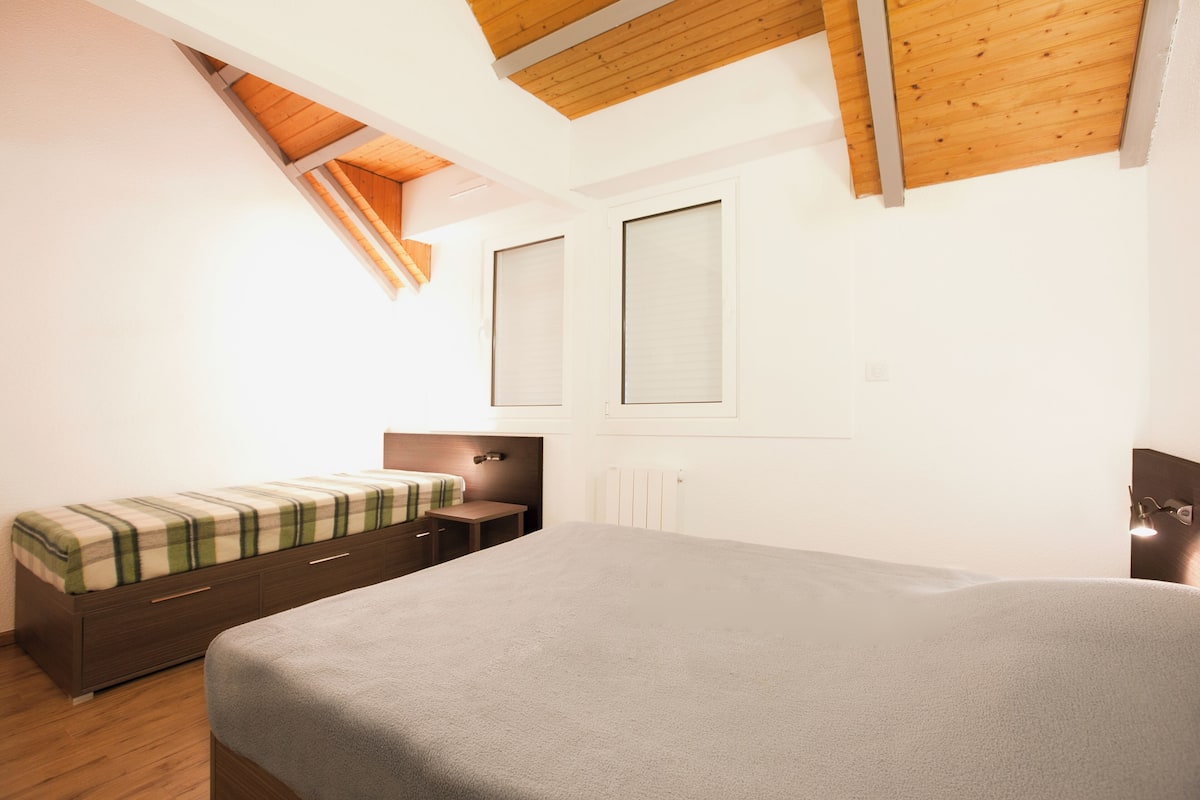 A bedroom with a bed, a nightstand, a dresser, and a window.