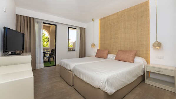 A hotel room with a bed, a TV, a desk, and a view of the outdoors. - Apartamentos Sinfony (Capdepera)