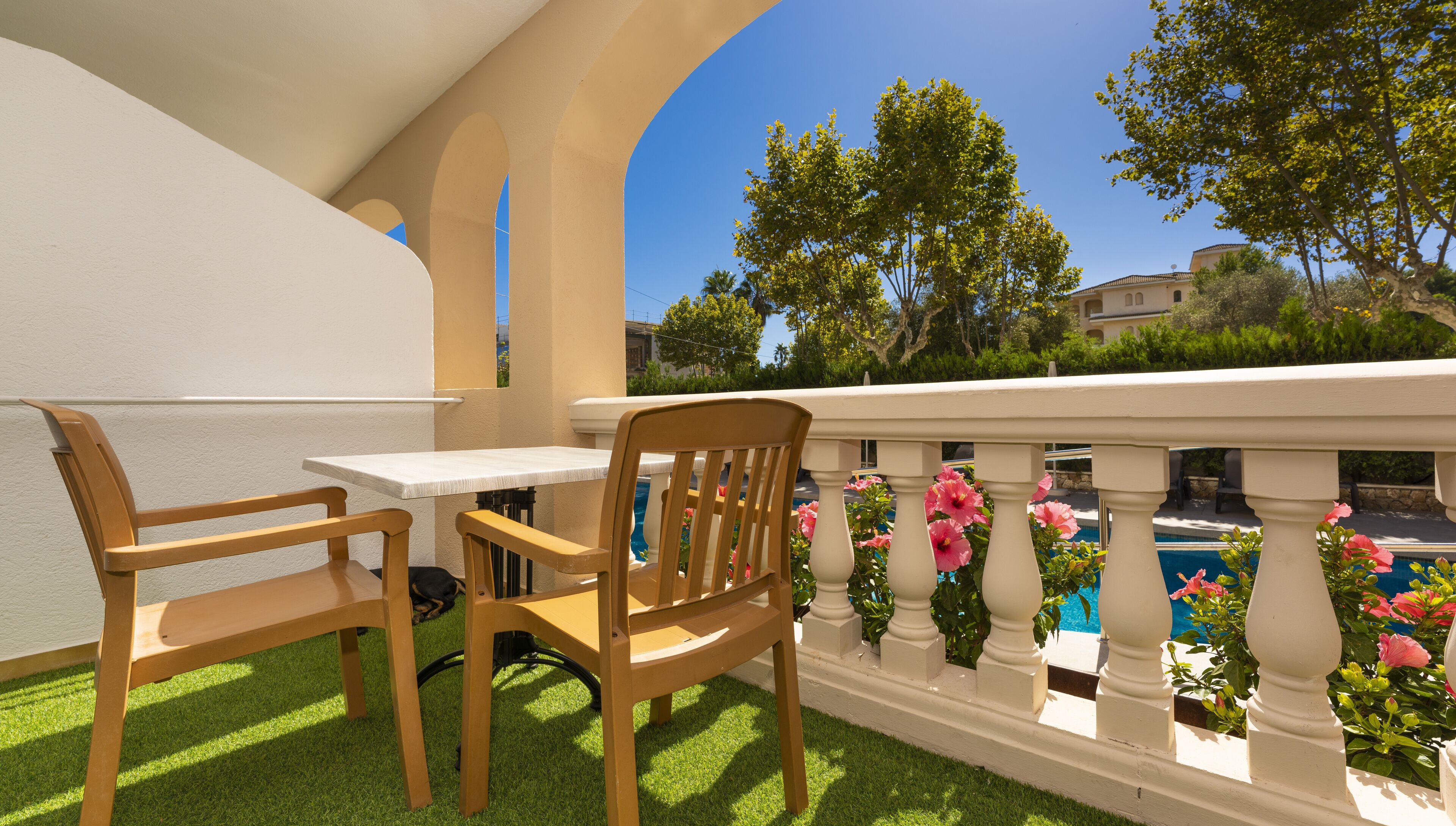 Un balcon avec une table et deux chaises, une piscine et de la verdure tout autour.