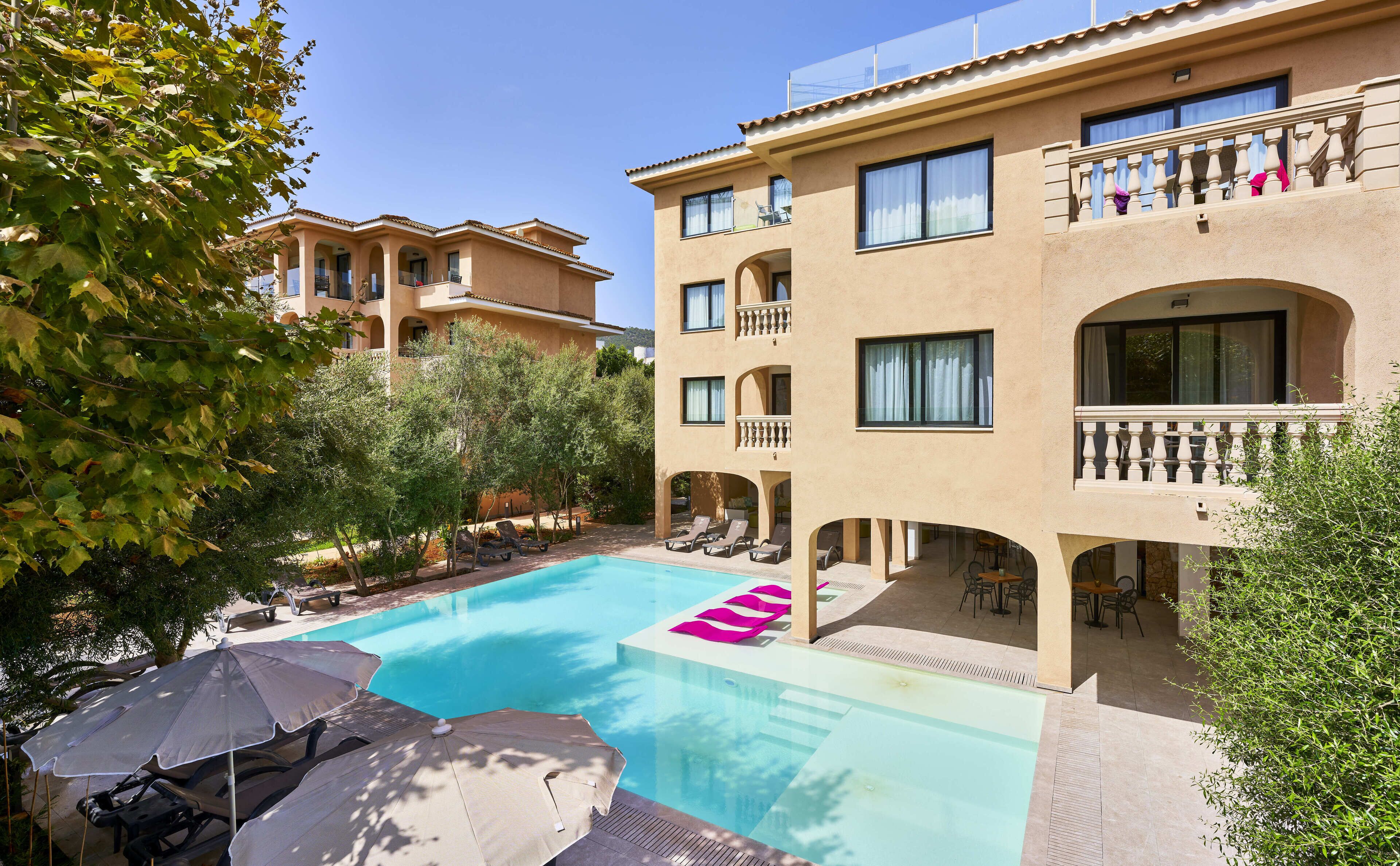 Un hotel con piscina, mobiliario exterior y varios balcones.