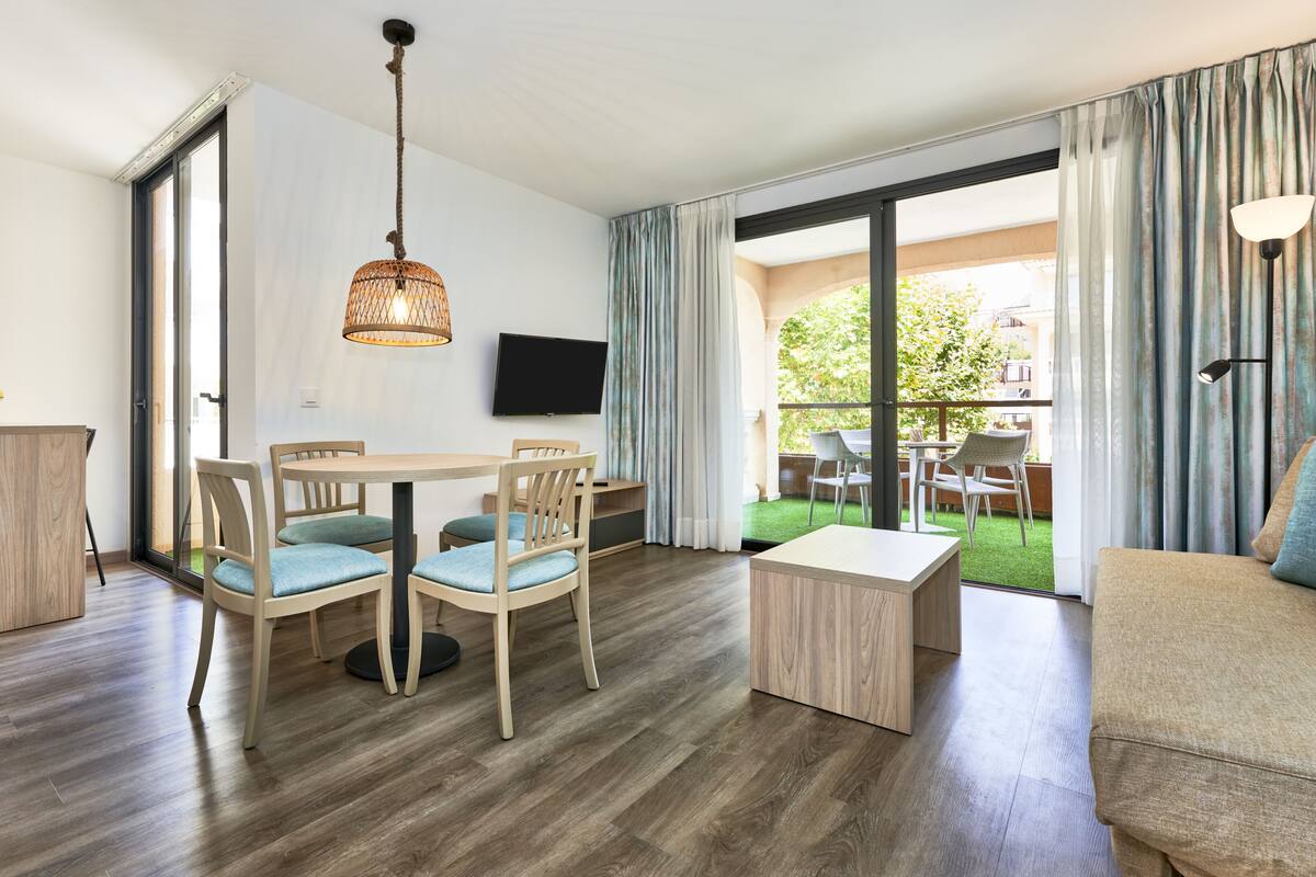 Una sala de estar moderna con una mesa de comedor de madera, dos sillas, un sofá y un televisor montado en la pared.