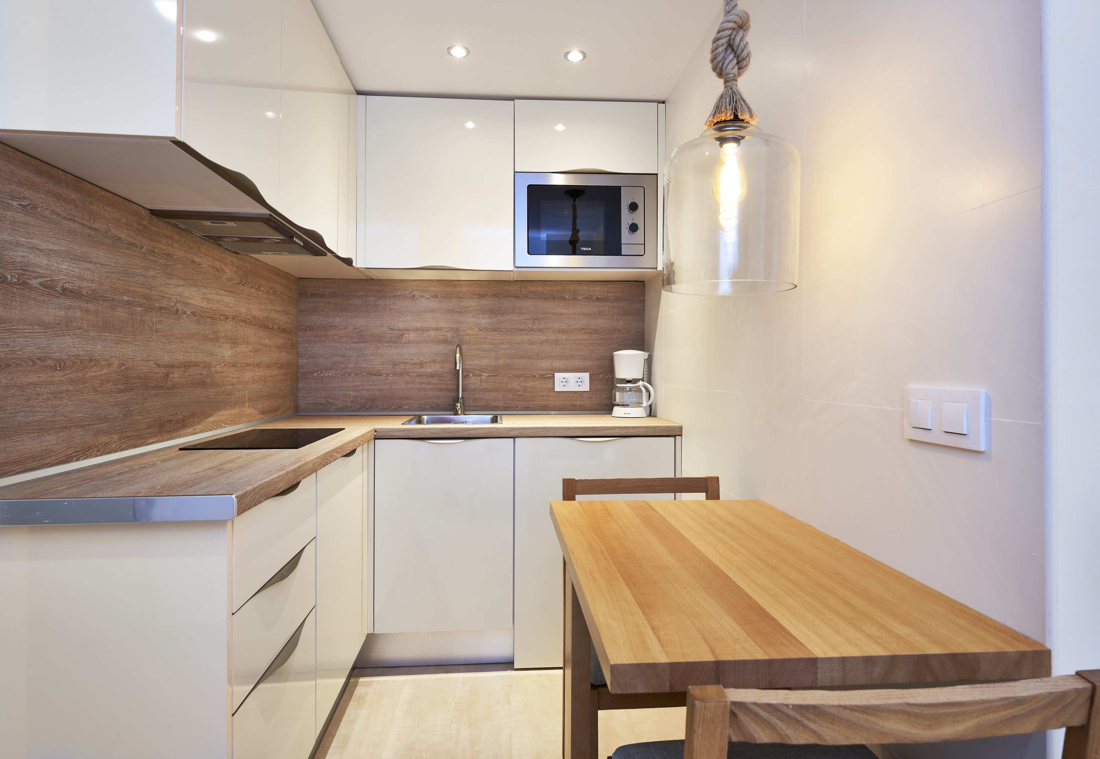 A modern kitchen with a wooden countertop, built-in cabinets, a stainless steel microwave, and a hanging light fixture.