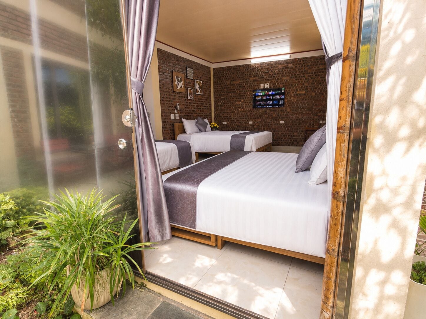 Una habitación con dos camas, un muro de ladrillo y una ventana con cortinas.