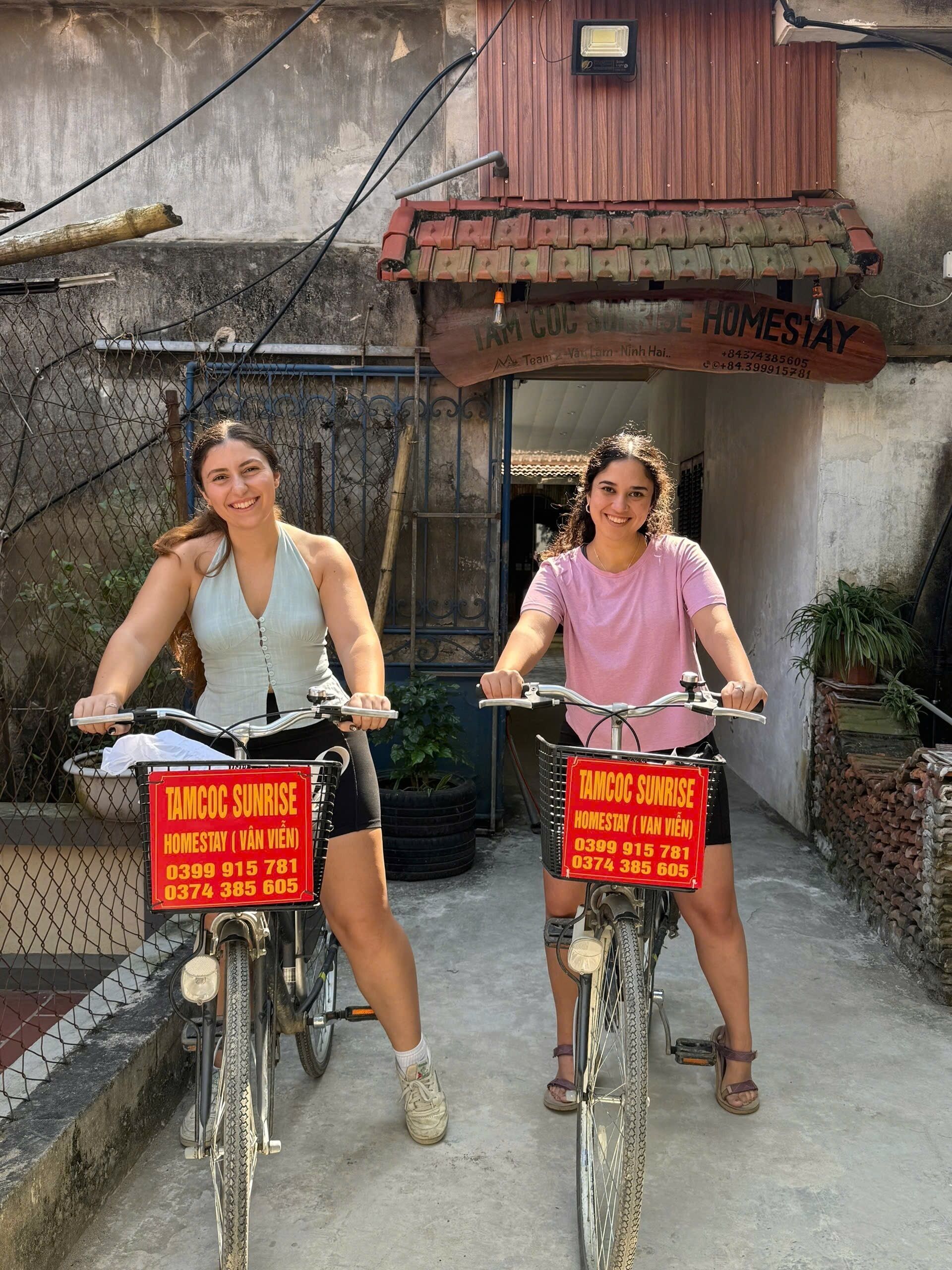 Two bicycles with signs advertising 'TAMCOC SUNRISE HOMESTAY (VAN VIEN)' and contact numbers.