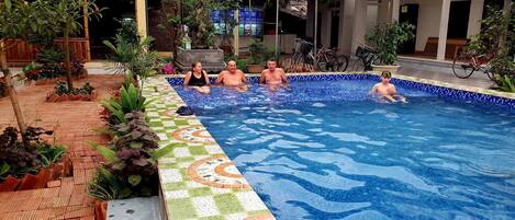 An indoor swimming pool with tiled edges, surrounded by potted plants and a tiled walkway.