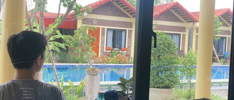 A person seated at a table with a view of a building with red roofs and a pool.