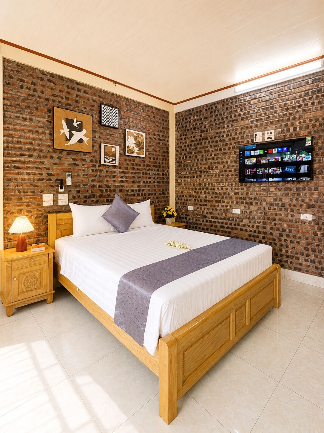 Ein Schlafzimmer mit Ziegelwand, einem Bett mit Holzrahmen, einem Nachttisch mit Lampe und einem an der Wand montierten Flachbildfernseher.