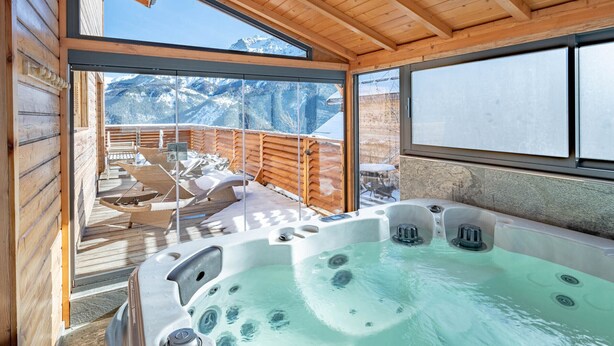 Eine Holzhütte mit Whirlpool, einer Holzterrasse und Blick auf schneebedeckte Berge.