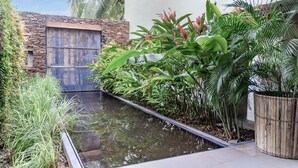 Un espace extérieur moderne agrémenté d’un élément aquatique, d’un mur en pierre et d’une végétation luxuriante.