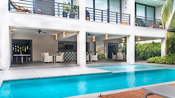 Un espace piscine moderne à plusieurs niveaux, doté d’un coin salon extérieur et offrant une vue sur une végétation luxuriante.