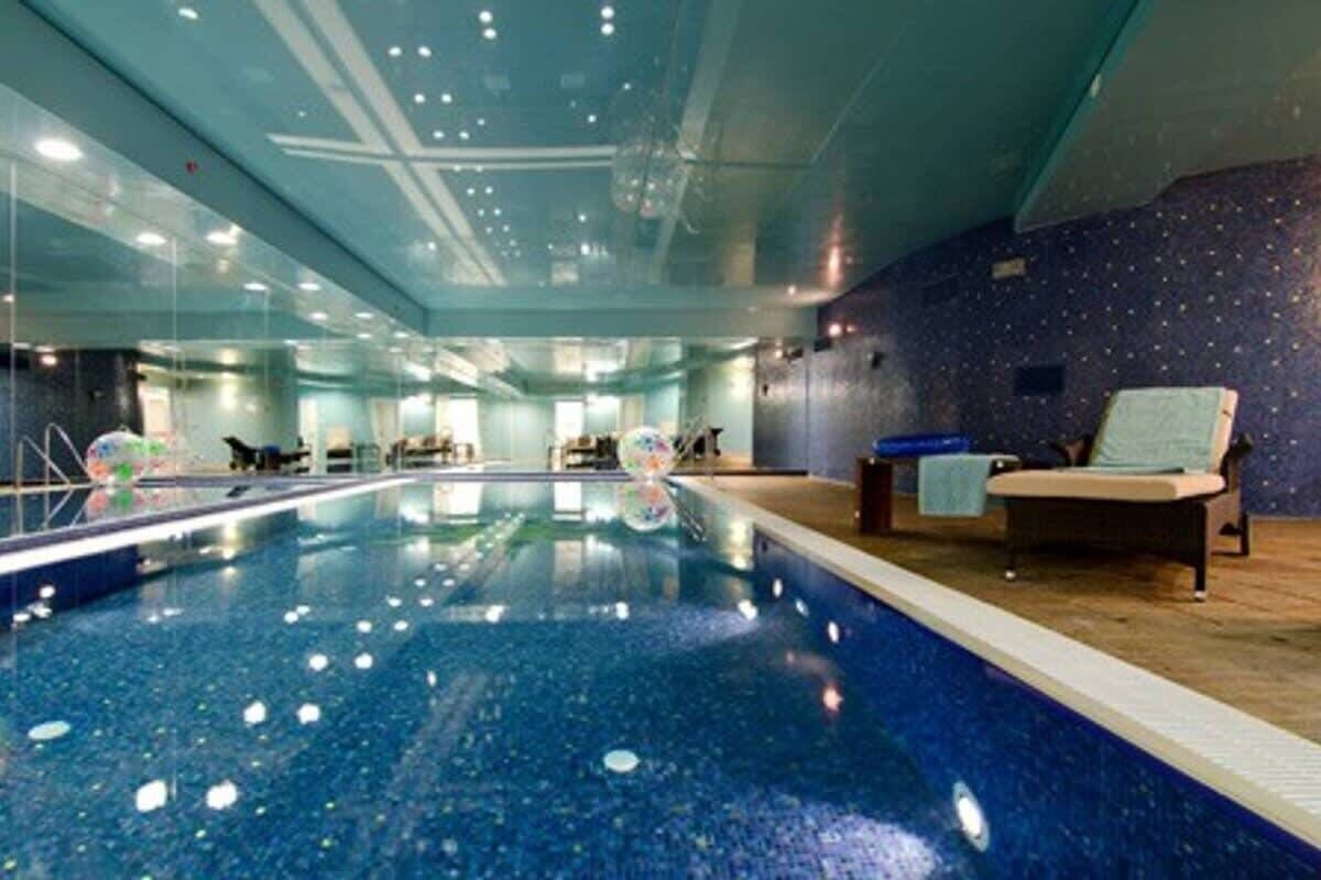 Ein überdachter Pool mit klarem, blauen Wasser, umgeben von Glaswänden und einem Holzboden.