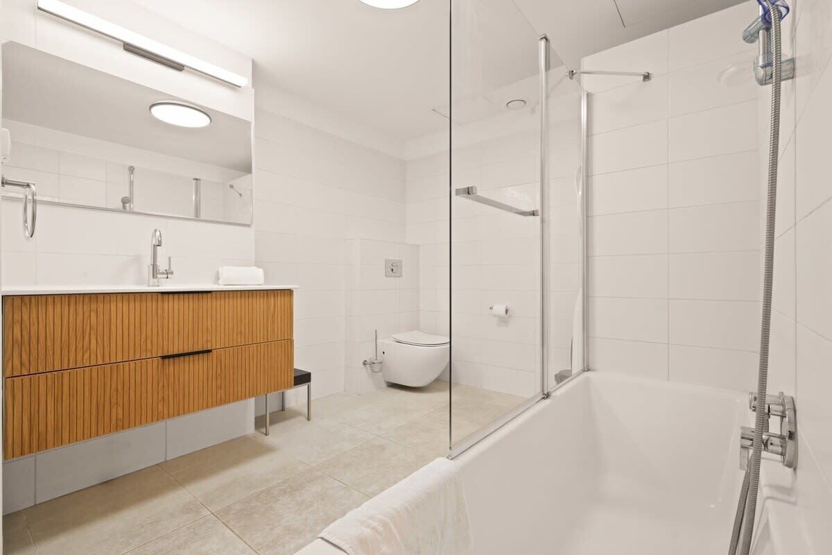 A modern bathroom with a glass-enclosed shower, a wooden vanity, and a white toilet.