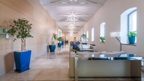 A spacious lobby with a modern design, featuring a central seating area, large potted plants, and a geometric ceiling design.
