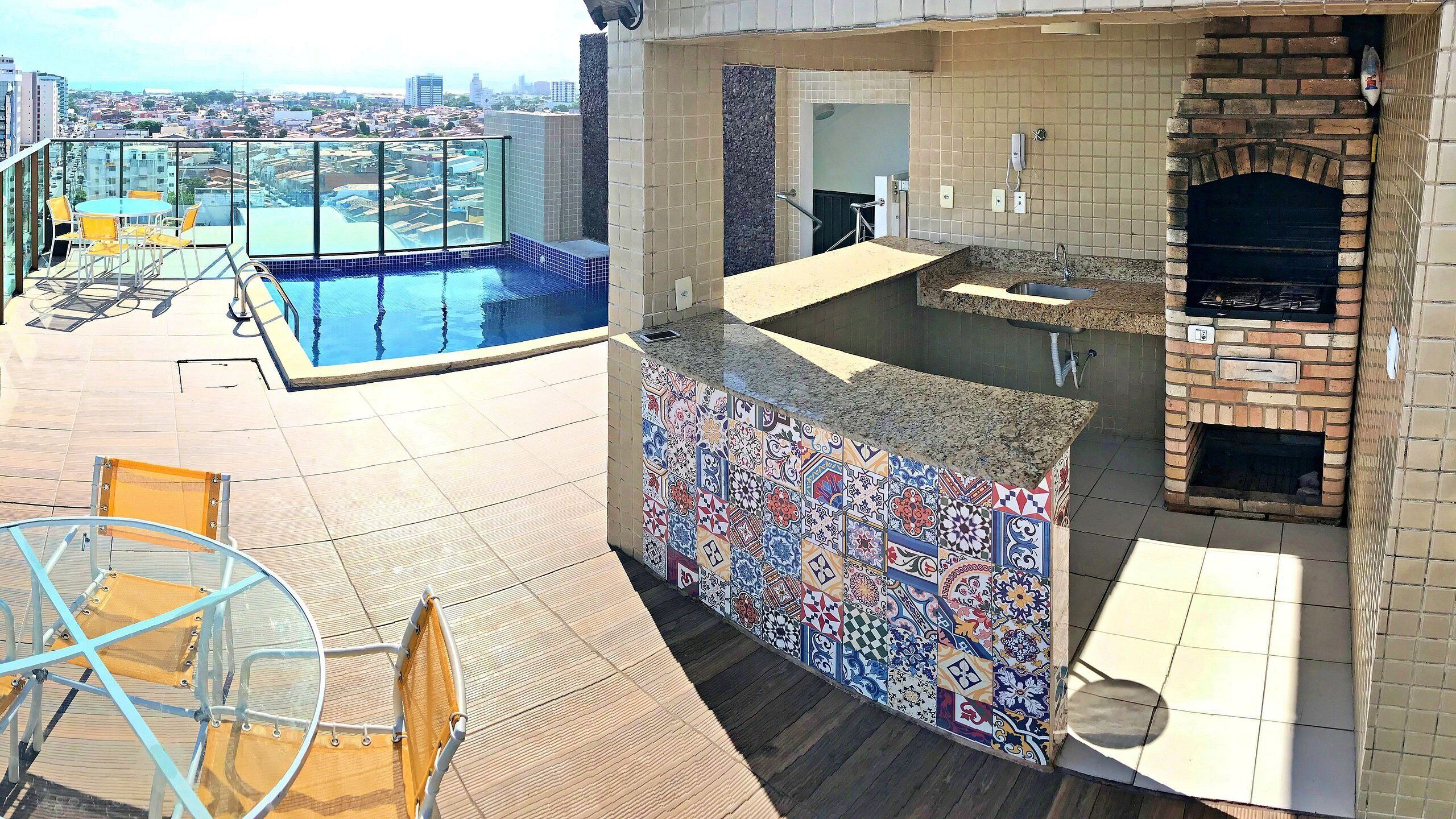 Et tag med swimmingpool, en glasgelænder, en terrasse med en farverig flisemur og en murstensovn.