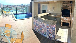 Un área de piscina en la azotea con barandilla de cristal, un patio con un muro de azulejos coloridos y un horno de ladrillo.