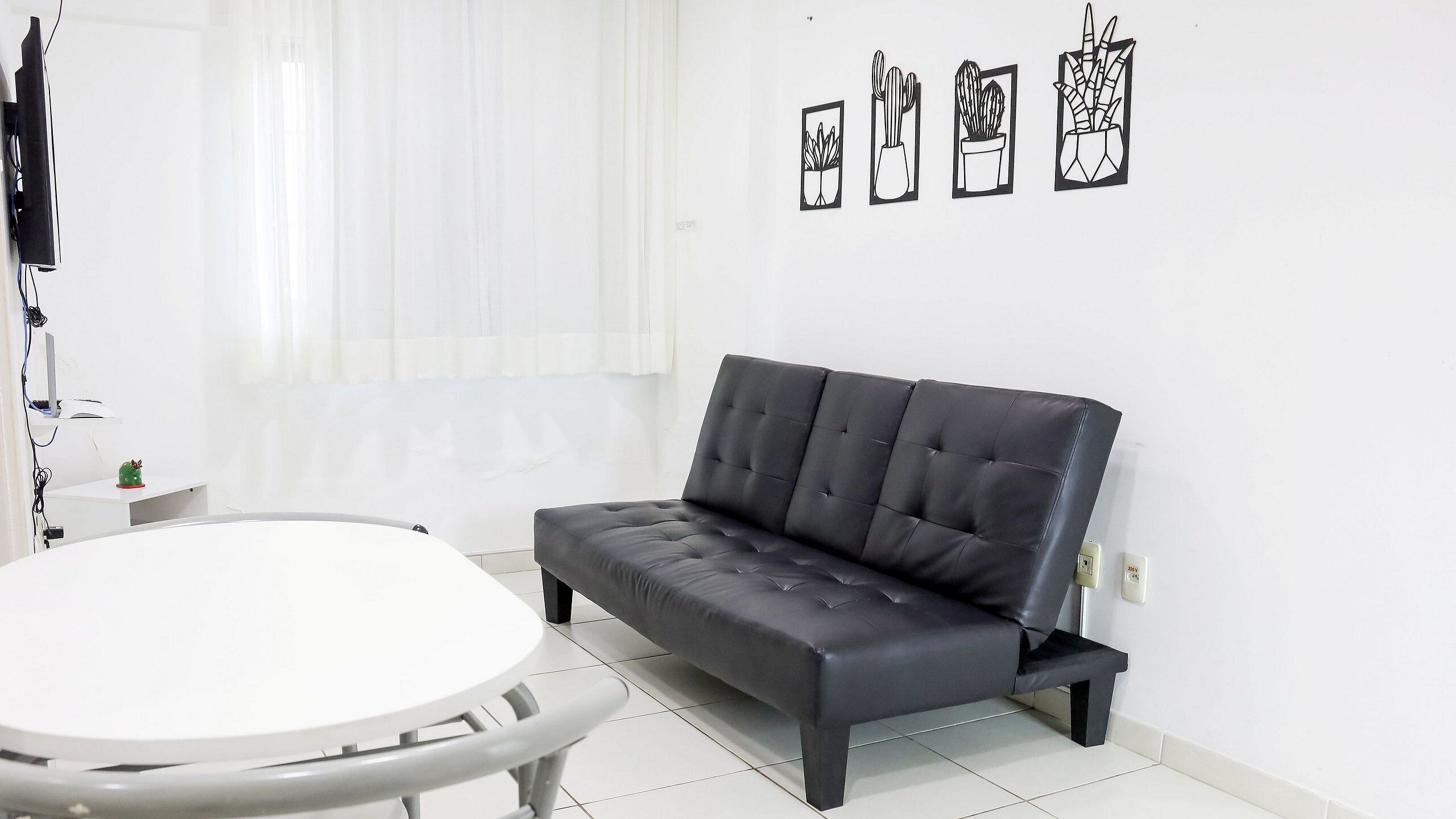 A modern living room with a black leather sofa, a round white table, and a wall-mounted TV.