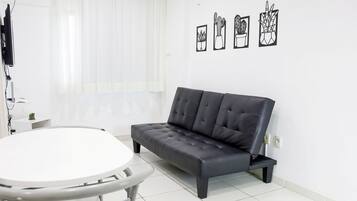 A modern living room with a black leather sofa, a round white table, and a wall-mounted TV.