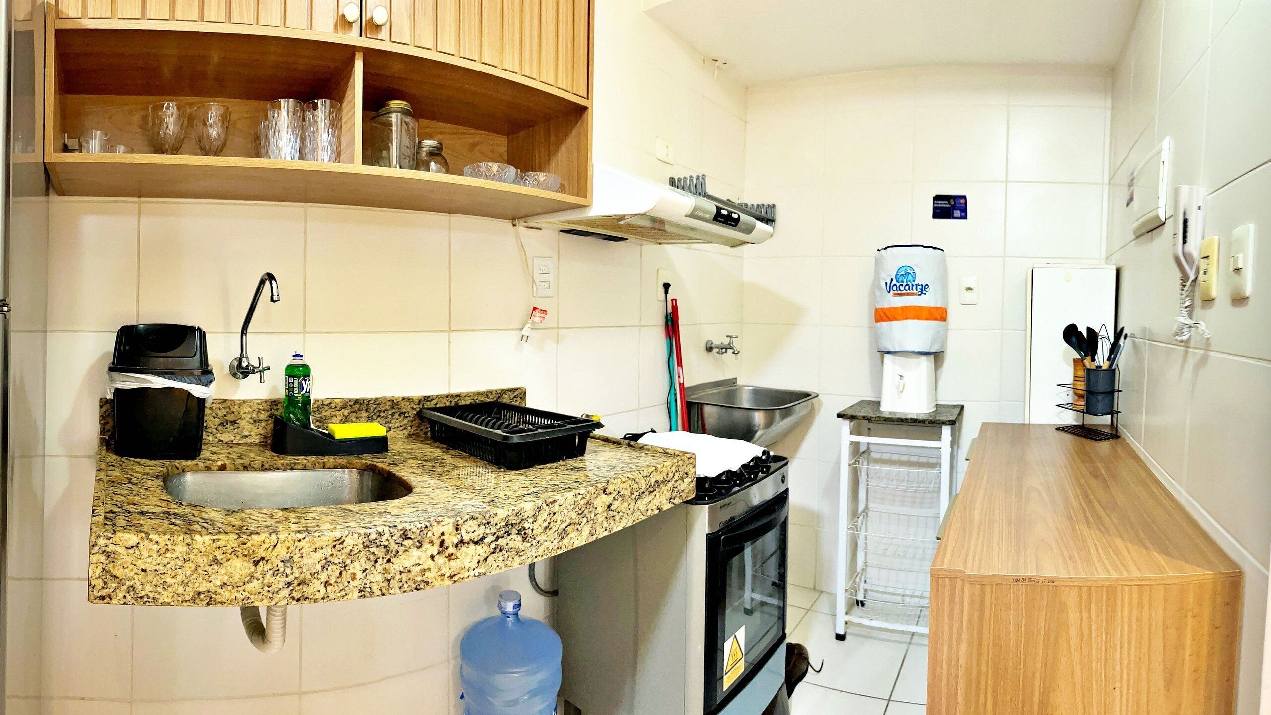 A compact kitchen with a granite countertop, a sink, a stove, and a water dispenser.