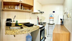 A compact kitchen with a granite countertop, a sink, a stove, and a water dispenser. - Vacanze - Gales da Pajuçara (Maceió)