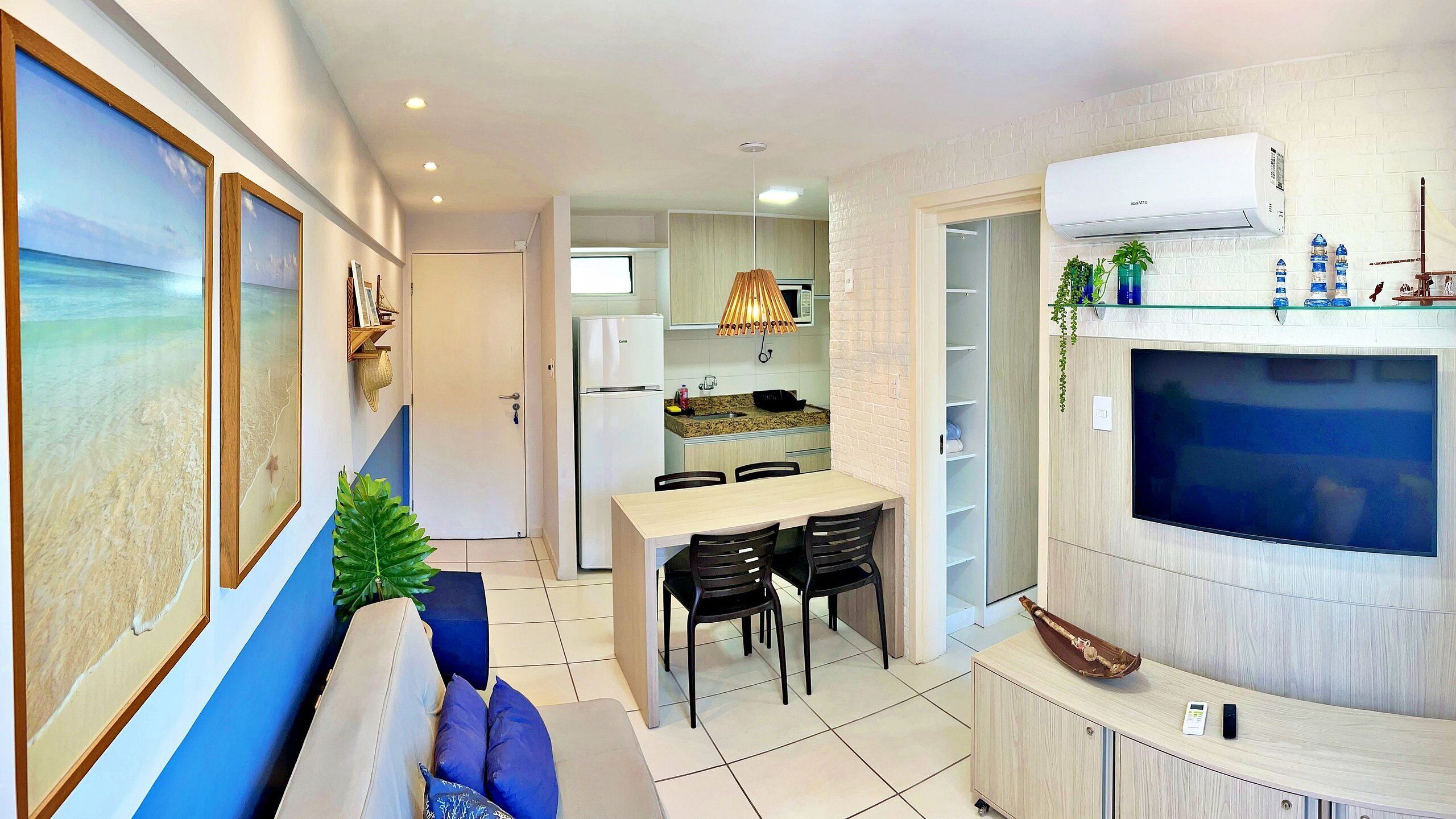 A modern kitchen with a dining area, a flat-screen TV, and a seating area with a view of the beach.