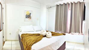 Un dormitorio con cama, ventana con cortinas, interruptor de luz en la pared y un cuadro enmarcado.
