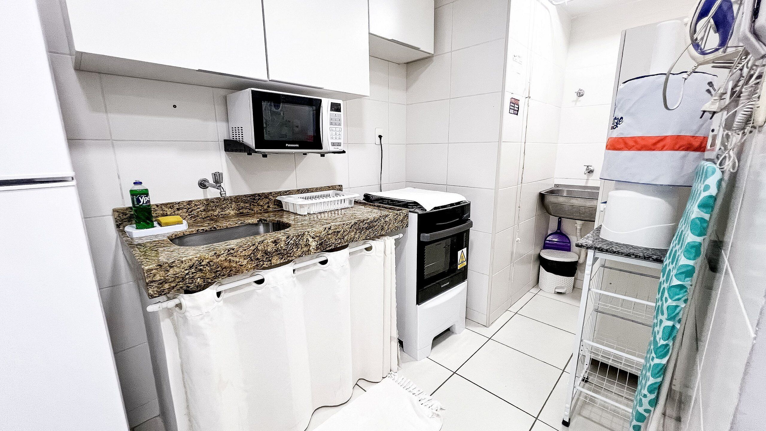 Cocina compacta con microondas, horno, fregadero y un pequeño cubo de basura.