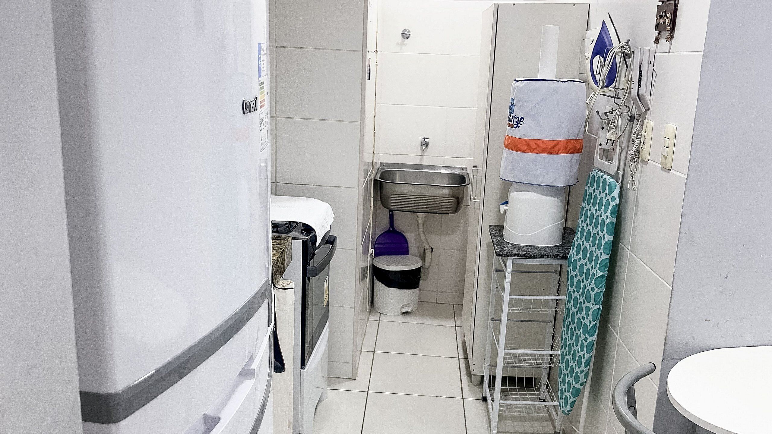 A narrow bathroom with a toilet, sink, and a small trash bin.
