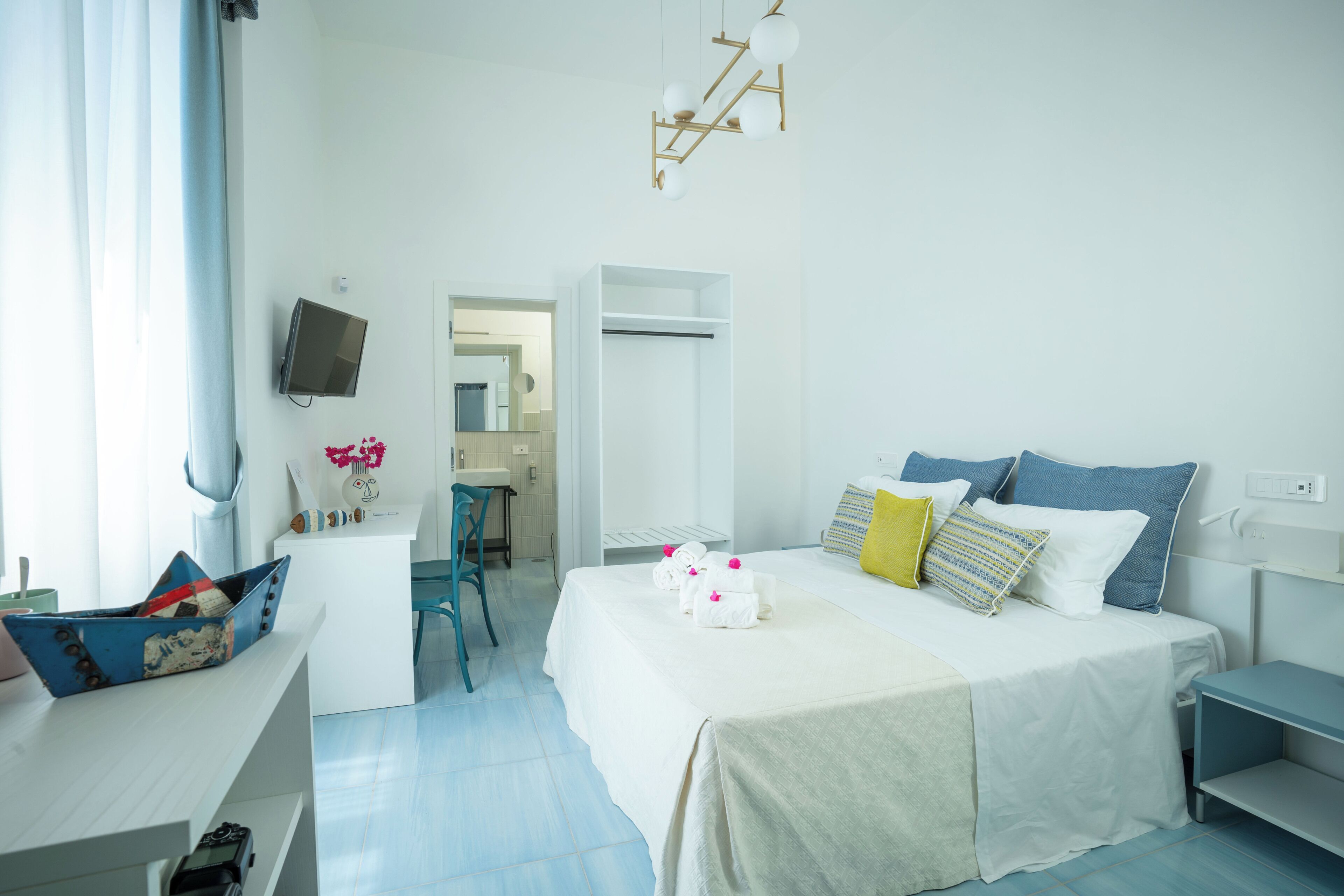 A modern hotel room with a bed, bedside tables, a desk, a chair, and a television.