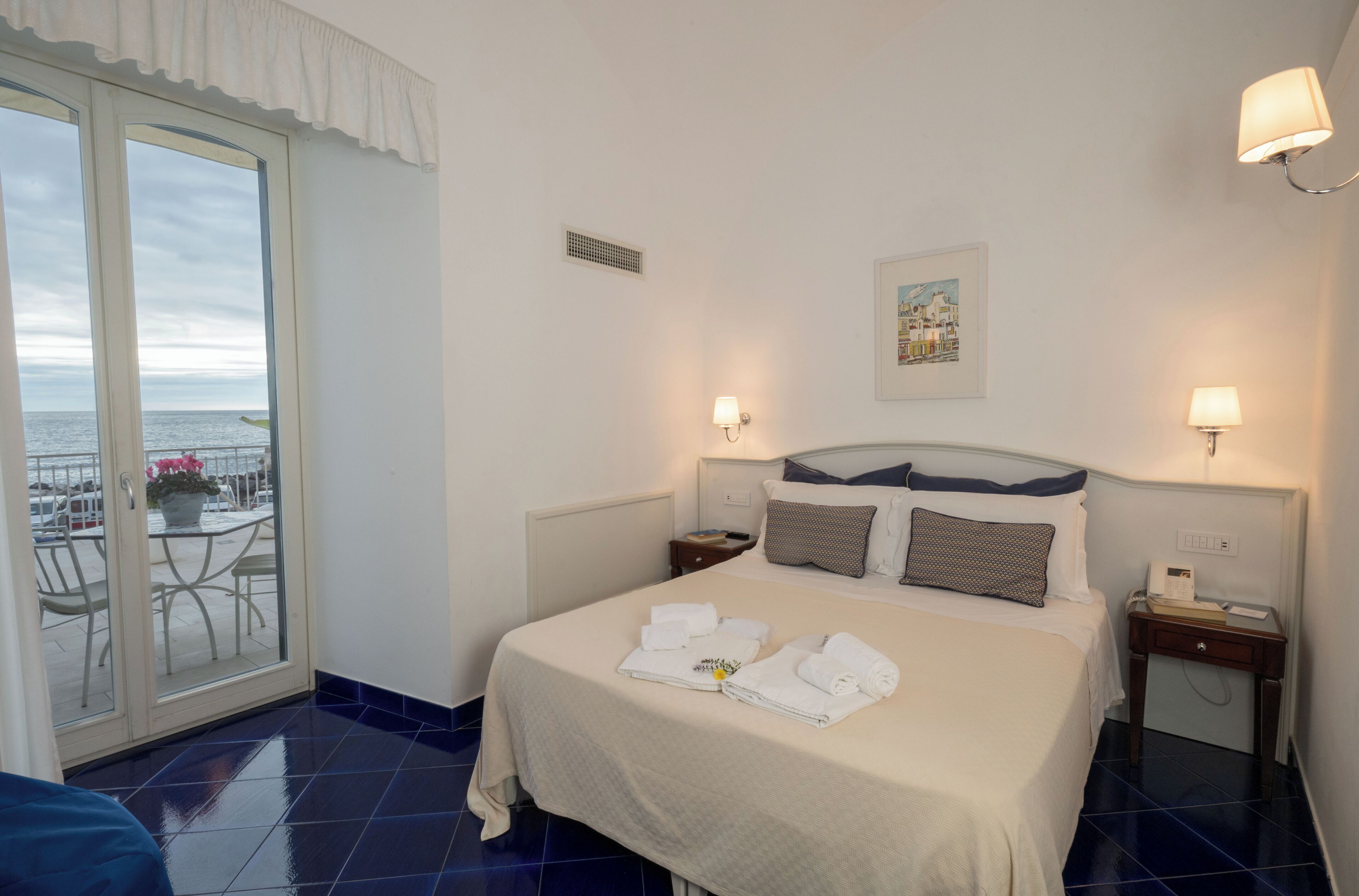 Una camera d'albergo con un letto, due comodini, una finestra vista e una porta che dà su un balcone.