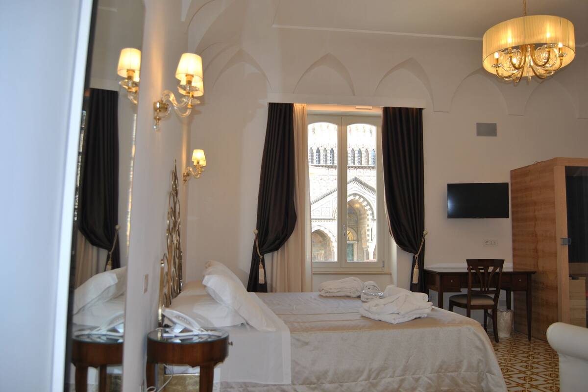 A hotel room with a bed, a desk, a chair, a TV, and a window with curtains.