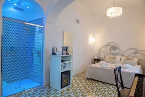 A hotel room with a shower, a bed, a nightstand, a mirror, and a chandelier. - Core Amalfitano City Suites (Amalfi)