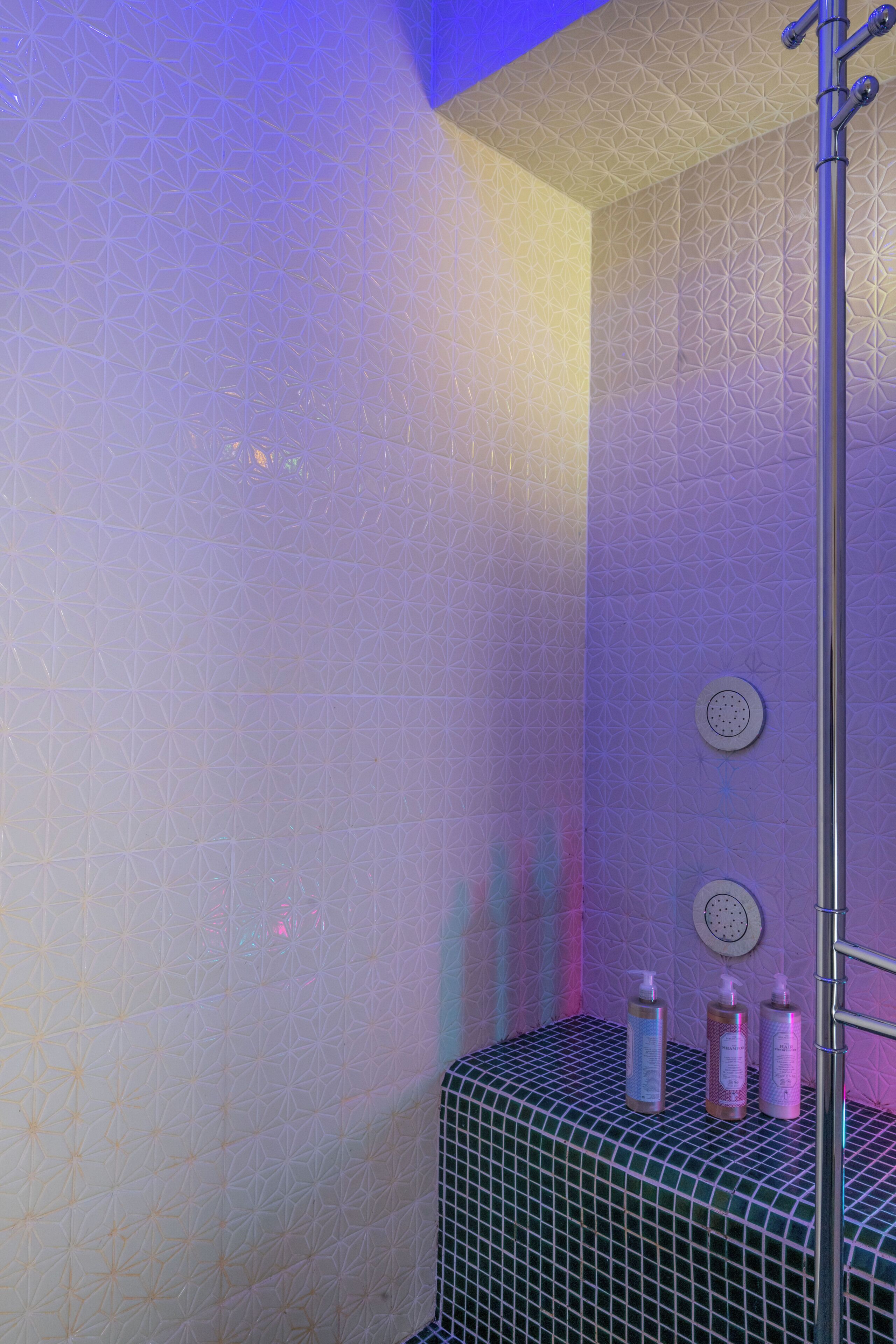 Ein Badezimmer mit Wandpaneelen mit geometrischem Muster, einer Duschkabine und Ablagefläche für Toilettenartikel.