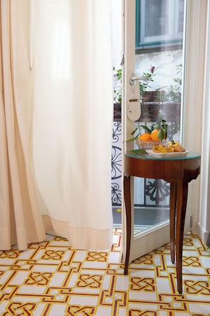 A room with a door leading to an outdoor area, a small table with a bowl of fruit, and patterned floor tiles. - Core Amalfitano City Suites (Amalfi)