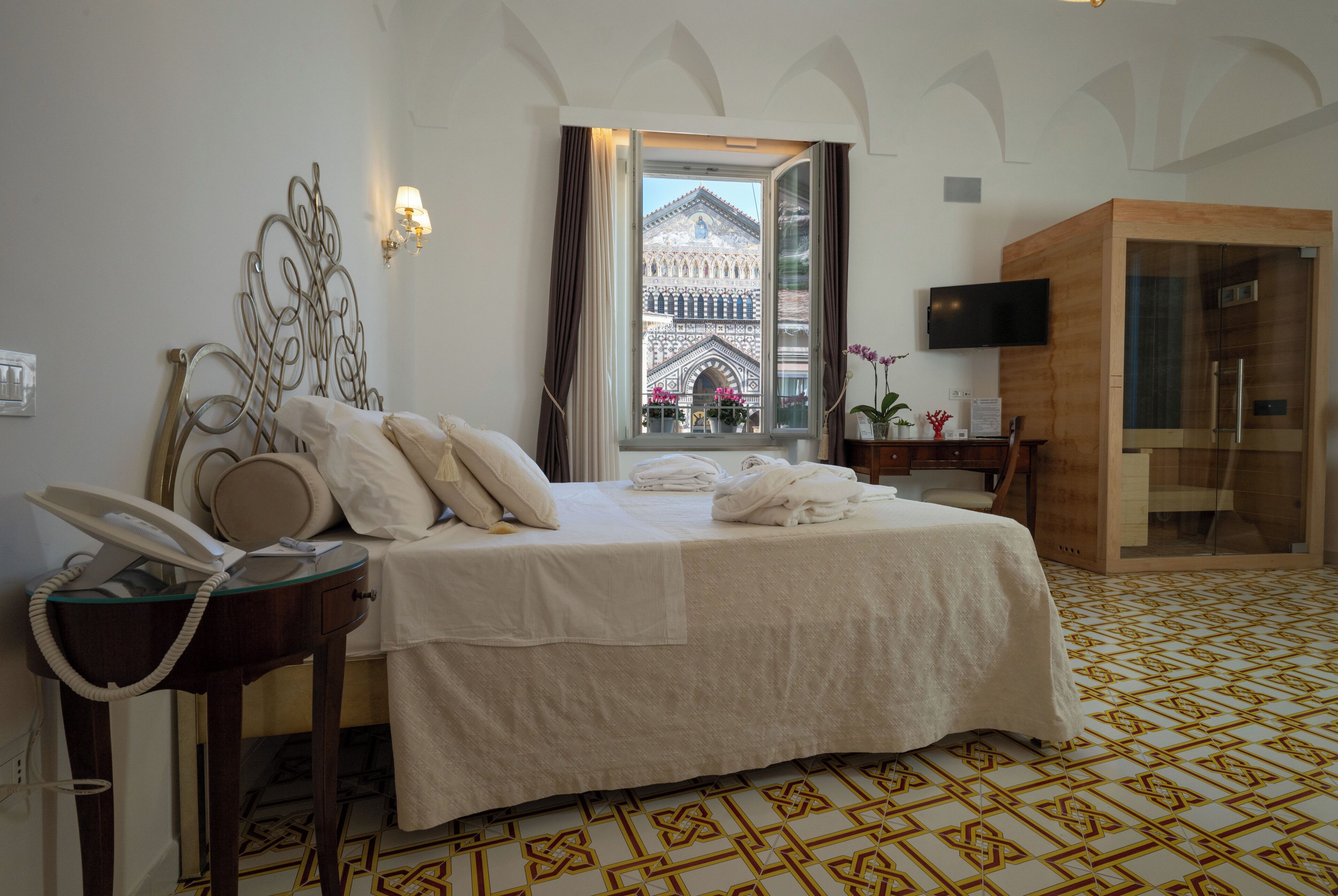 A hotel room with a bed, a telephone, a TV, a bathroom, and a view of a building outside.