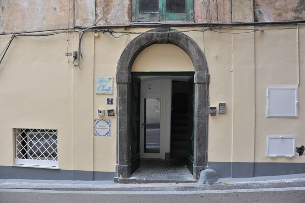 A building entrance with an arched doorway, a small window with a metal grille, and a door with a glass panel. - Core Amalfitano City Suites (Amalfi)
