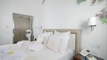 A hotel room with a bed, a bedside table with a phone and books, a wall-mounted lamp, and a shower area.
