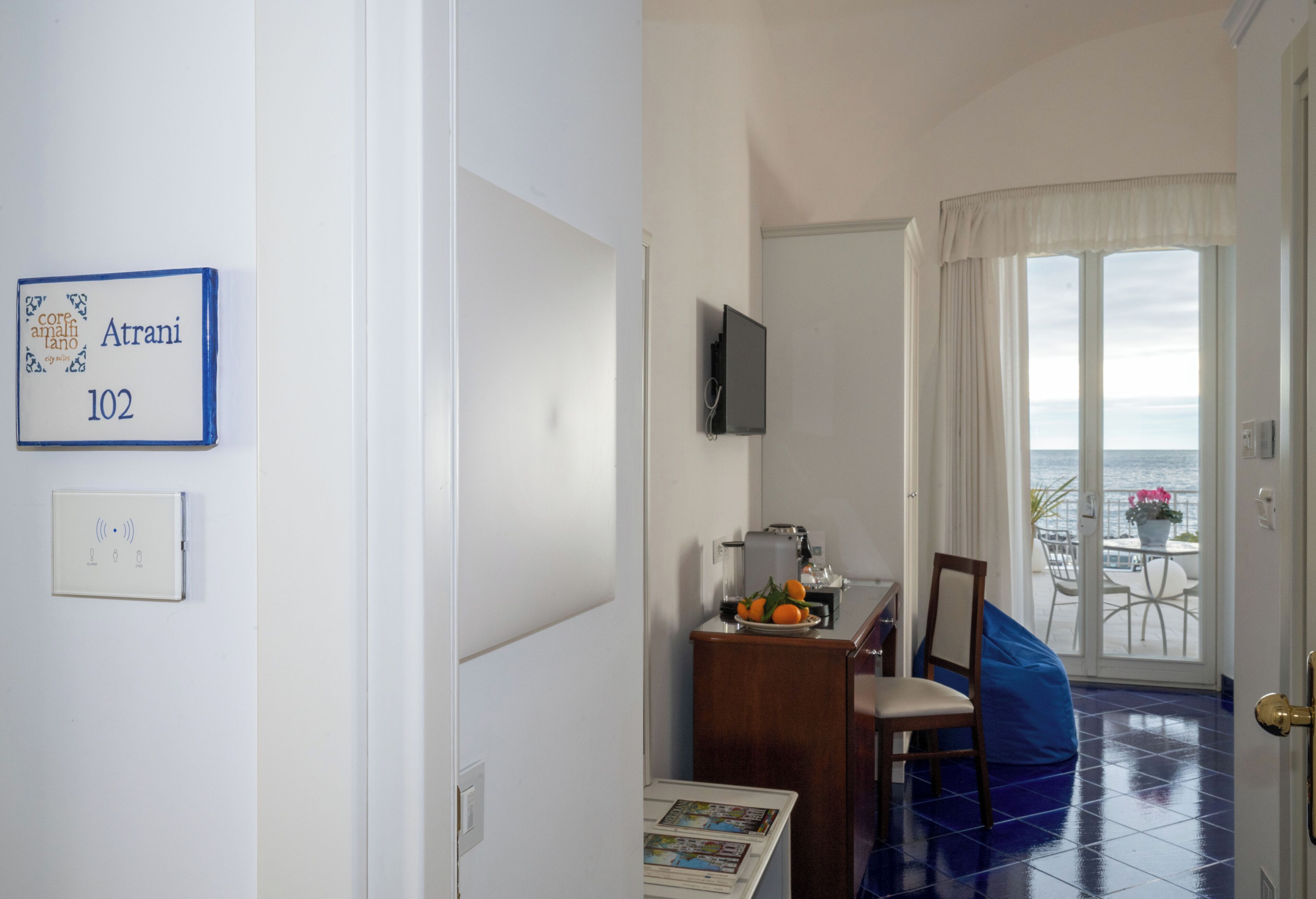 Una stanza con vista mare, una televisione a parete e un tavolo con arance e una macchina per il caffè.