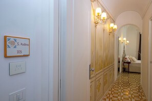 Un pasillo con un letrero que indica la habitación 105, un interruptor de luz y una puerta que da a una habitación con una cama y una mesa.