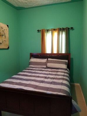 Uma cama de solteiro com estrutura de madeira e roupa de cama listrada em quarto com paredes verdes.