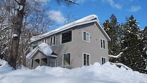 Una casa de dos pisos con techo inclinado, rodeada de nieve y árboles.