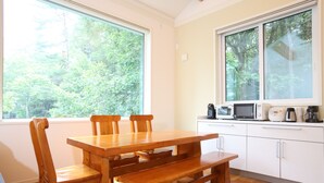 Una mesa de comedor de madera con bancos, un microondas y una cafetera sobre una encimera blanca.