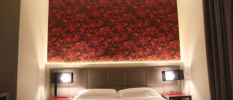 A hotel room with a large bed, two bedside tables, and a wall with a red floral pattern.
