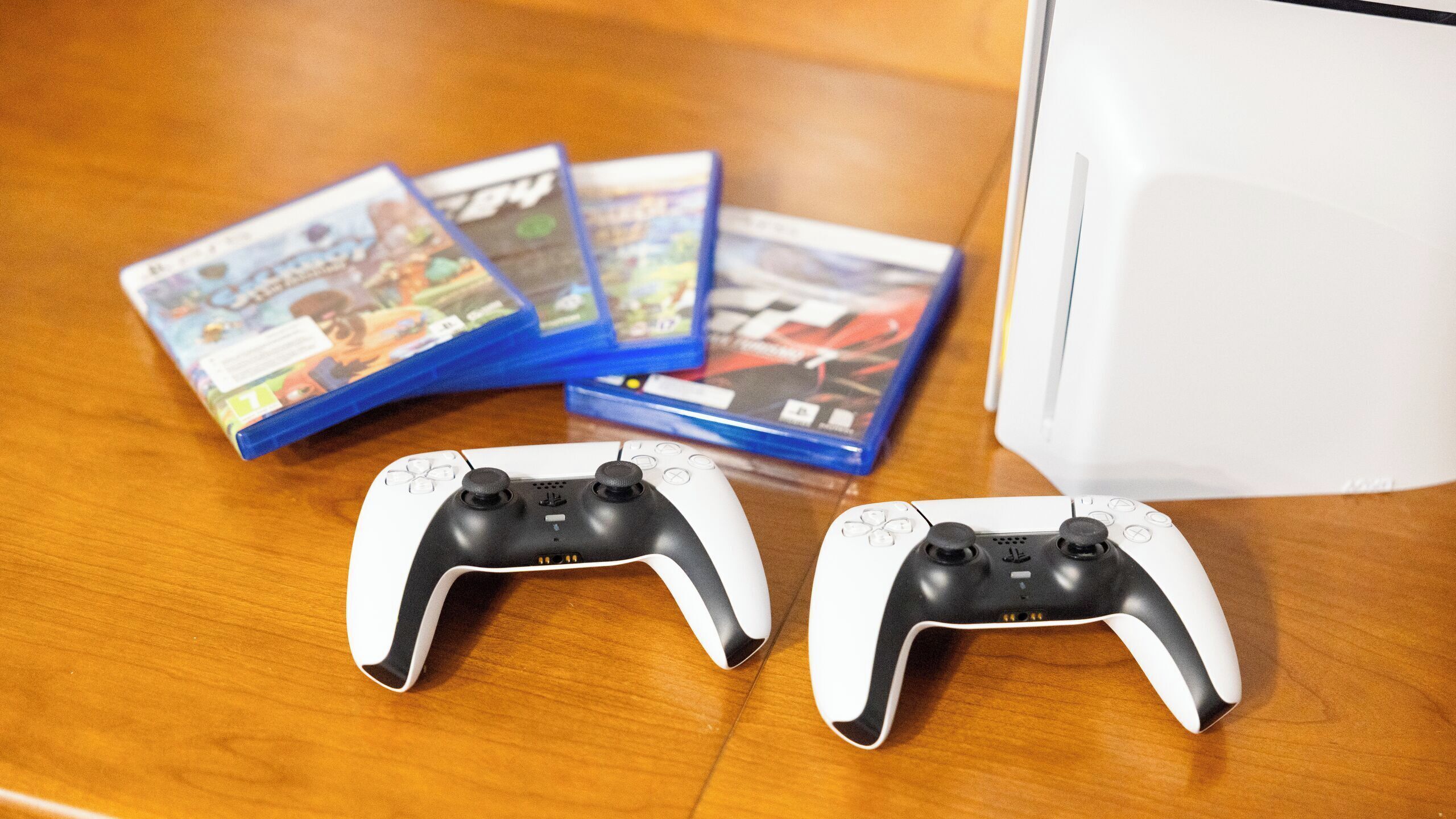 Dos controles blancos y negros sobre una superficie de madera con varias cajas de videojuegos.